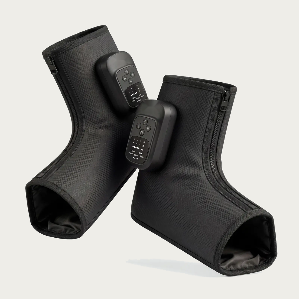 NACRE FORM™ cordless air compression foot and ankle massager displayed as a pair of black wearable massage boots against a warm cream background. Each electric foot massager features a textured fabric exterior, integrated digital control panel, adjustable massage functions and front zip fastening. The product photograph presents a rechargeable heated foot massage device with comfortable ankle coverage, portable construction and personalised compression settings for convenient home relaxation.