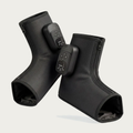 NACRE FORM™ cordless air compression foot and ankle massager displayed as a pair of black wearable massage boots against a warm cream background. Each electric foot massager features a textured fabric exterior, integrated digital control panel, adjustable massage functions and front zip fastening. The product photograph presents a rechargeable heated foot massage device with comfortable ankle coverage, portable construction and personalised compression settings for convenient home relaxation.