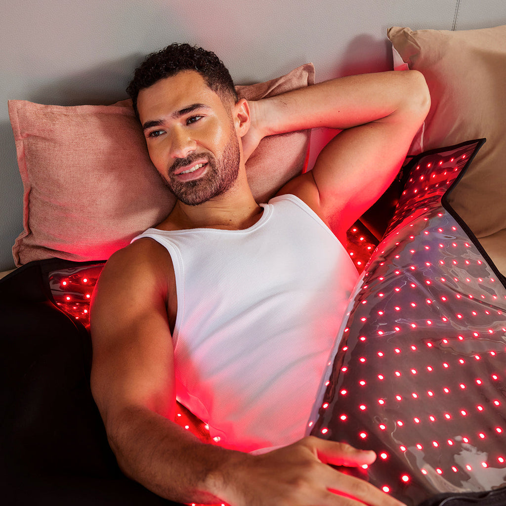 Man relaxing in bed using the NACRE FORM™ Full Body Red Light Therapy Blanket, a flexible wraparound LED therapy blanket with glowing red lights, designed for comfortable full-body red light and near-infrared wellness sessions at home.